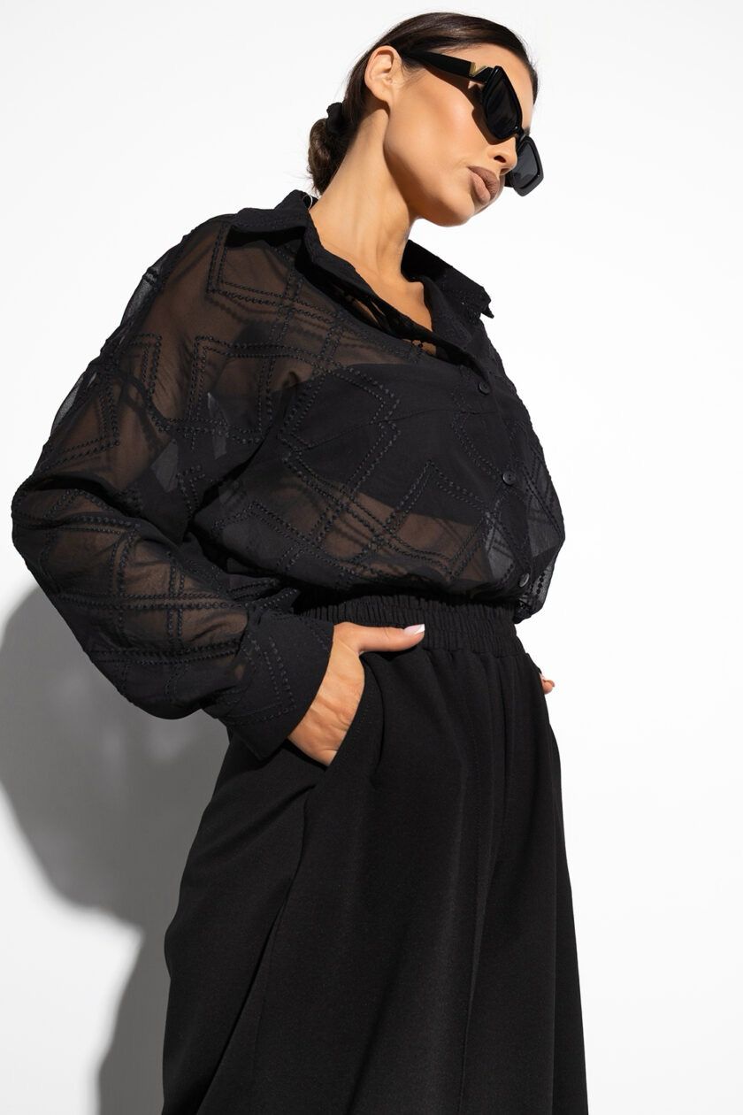 Czarna, półprzezroczysta koszula oversize na guziki, z długimi rękawami zakończonymi mankietami. Wykonana z lekkiego materiału, luźno układa się na sylwetce, dodając stylizacji eleganckiego luzu. Jednolity kolor i prosty krój sprawiają, że pasuje zarówno do codziennych, jak i wieczorowych outfitów.