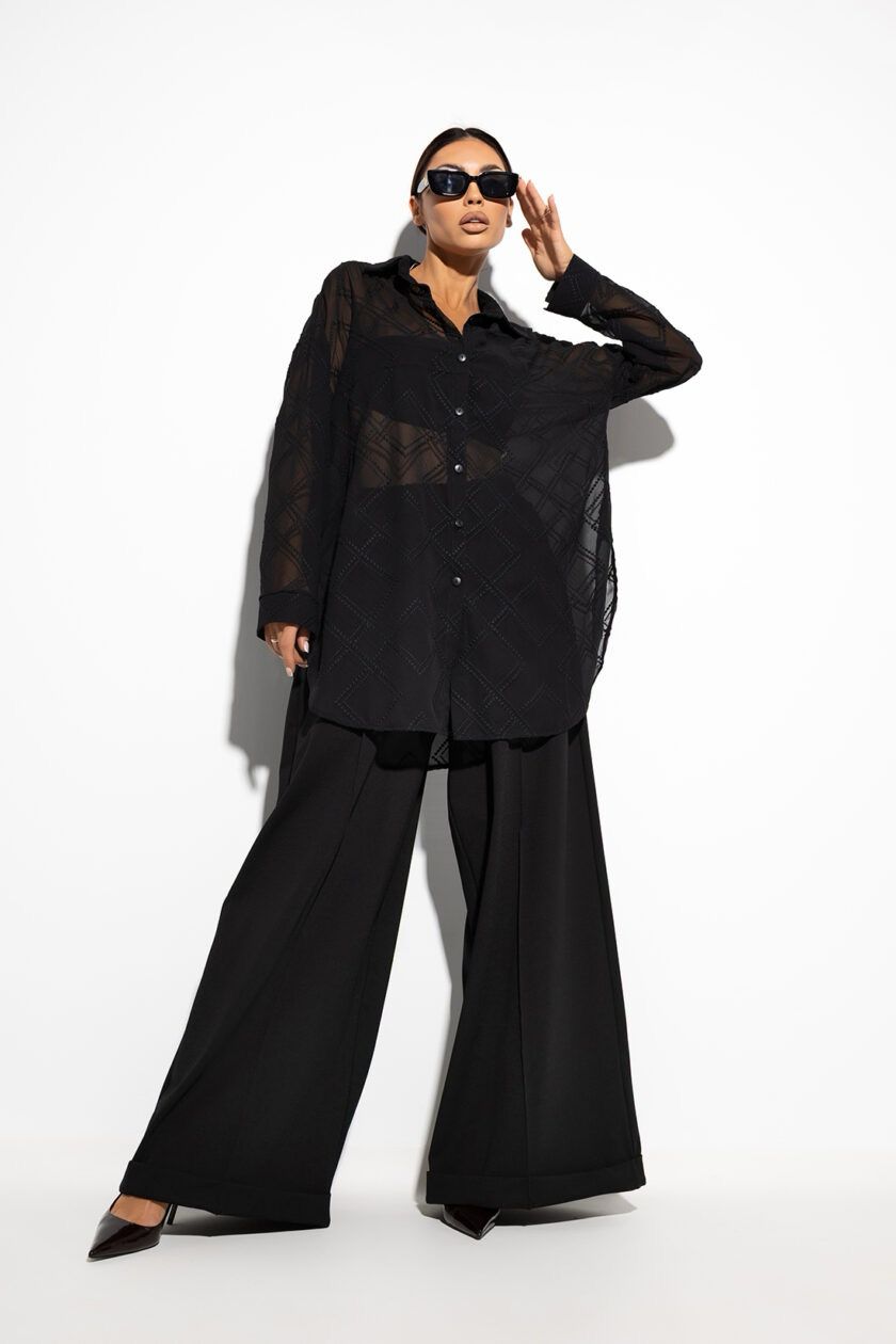 Czarna, półprzezroczysta koszula oversize na guziki, z długimi rękawami zakończonymi mankietami. Wykonana z lekkiego materiału, luźno układa się na sylwetce, dodając stylizacji eleganckiego luzu. Jednolity kolor i prosty krój sprawiają, że pasuje zarówno do codziennych, jak i wieczorowych outfitów.